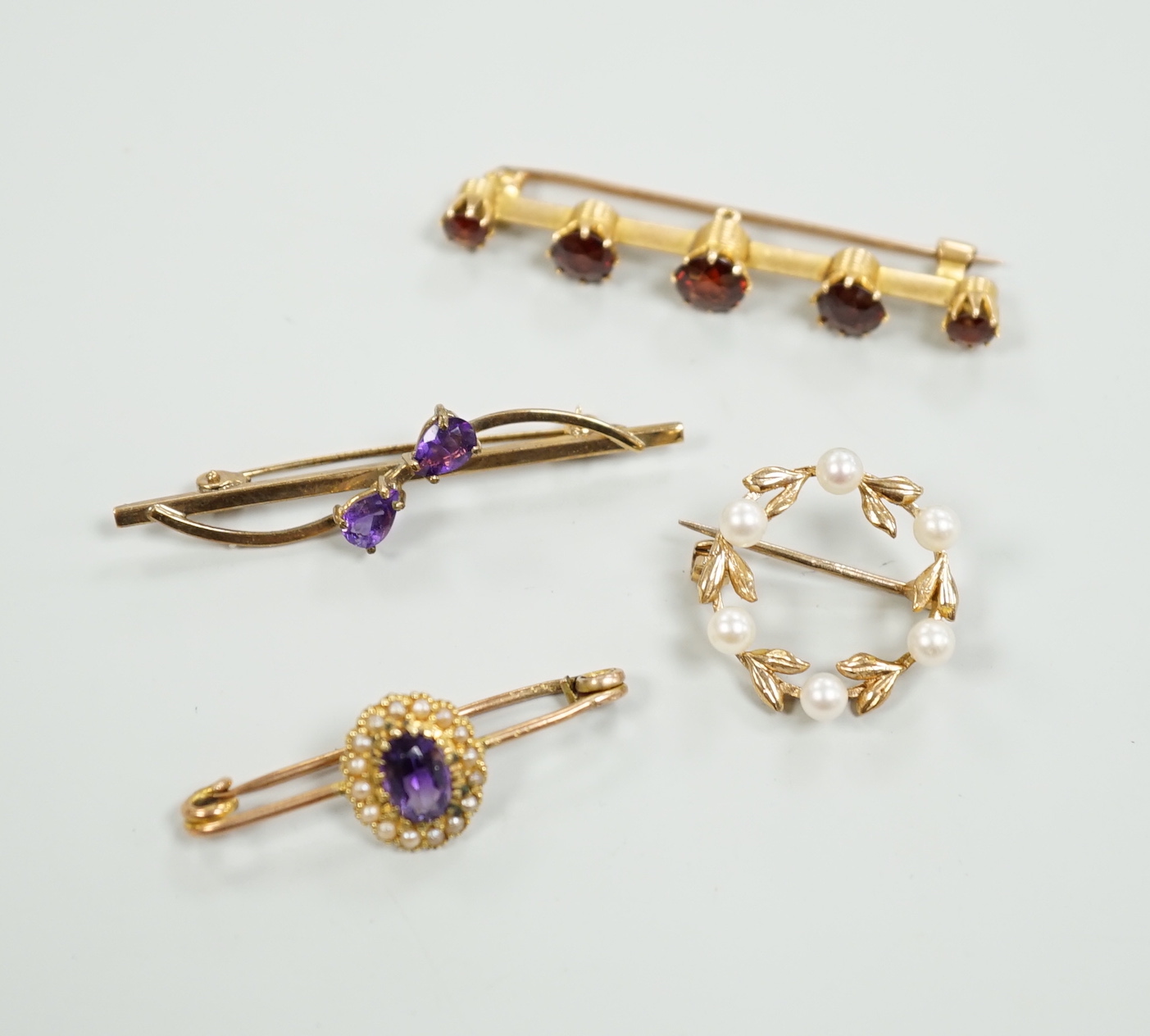 A 15ct and graduated five stone garnet set bar brooch, 48mm, a similar amethyst and seed pearl cluster set brooch and two other gem set brooches, including 9ct gold.